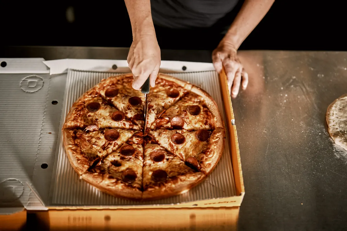 En pepperonipizza blir delt i stykker i en Dolly-eske