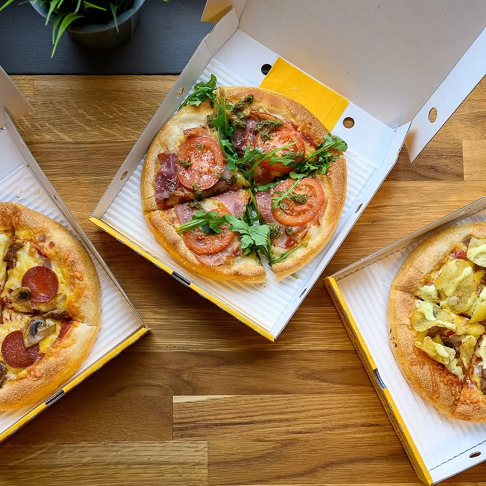 Tre Dolly-pizzaer i åpne esker på et trebord, sett ovenfra
