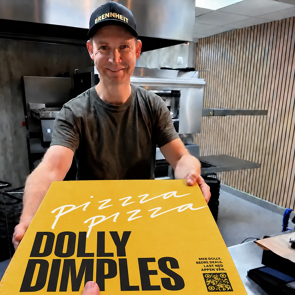 En smilende Dolly-ansatt rekker frem en gul Dolly Dimples-pizzaeske