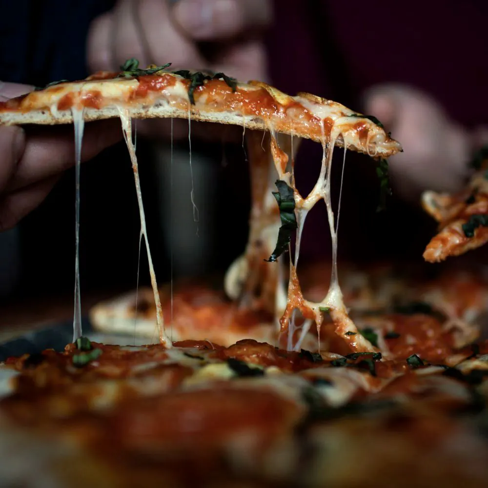 Hender løfter pizzastykker med lange tråder av smeltet ost