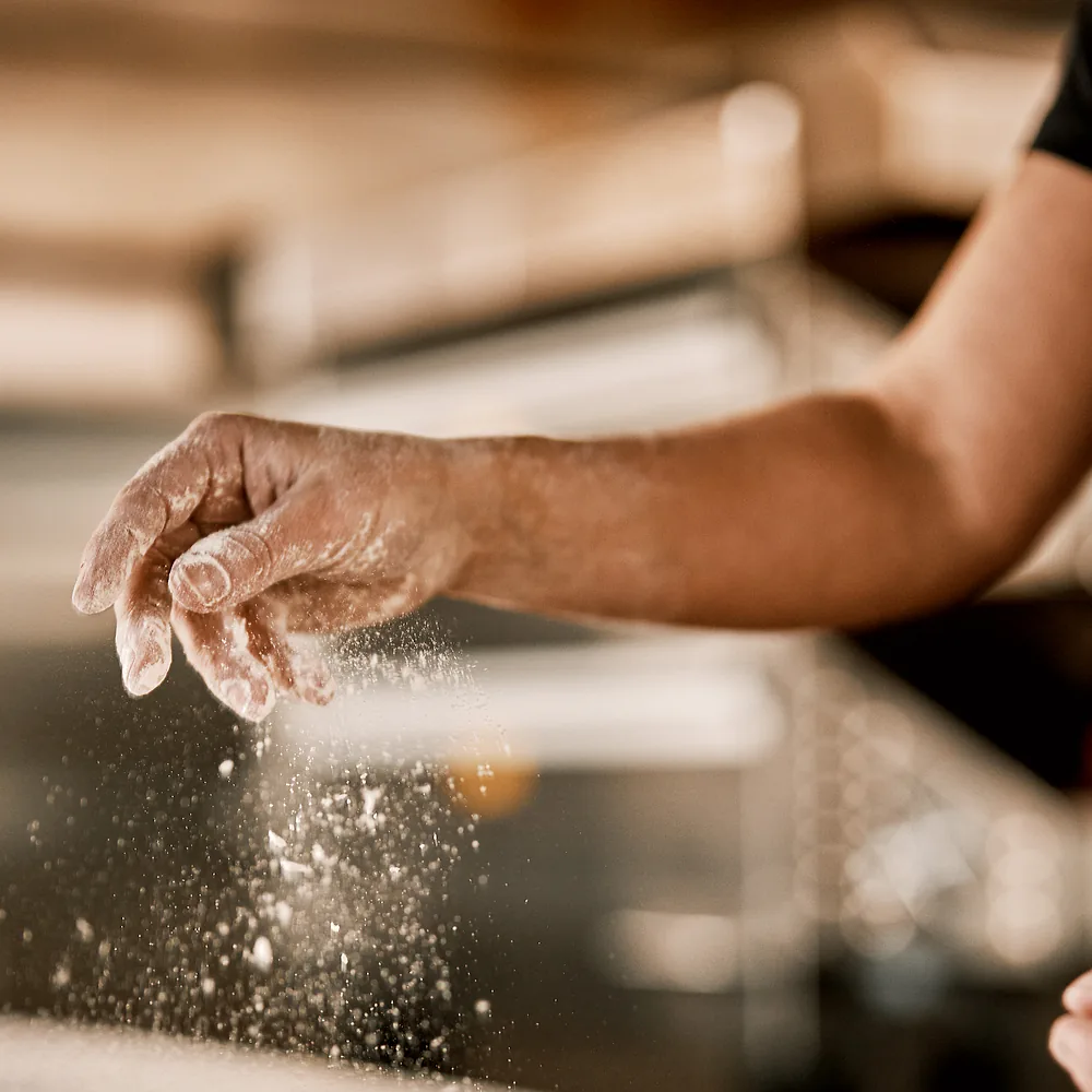 En pizzabaker drysser mel over deigen
