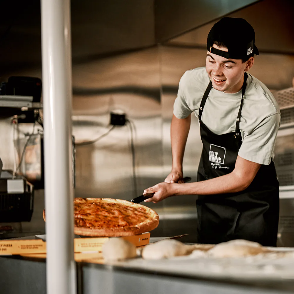En smilende pizzabaker med en nystekt pizza på spaden