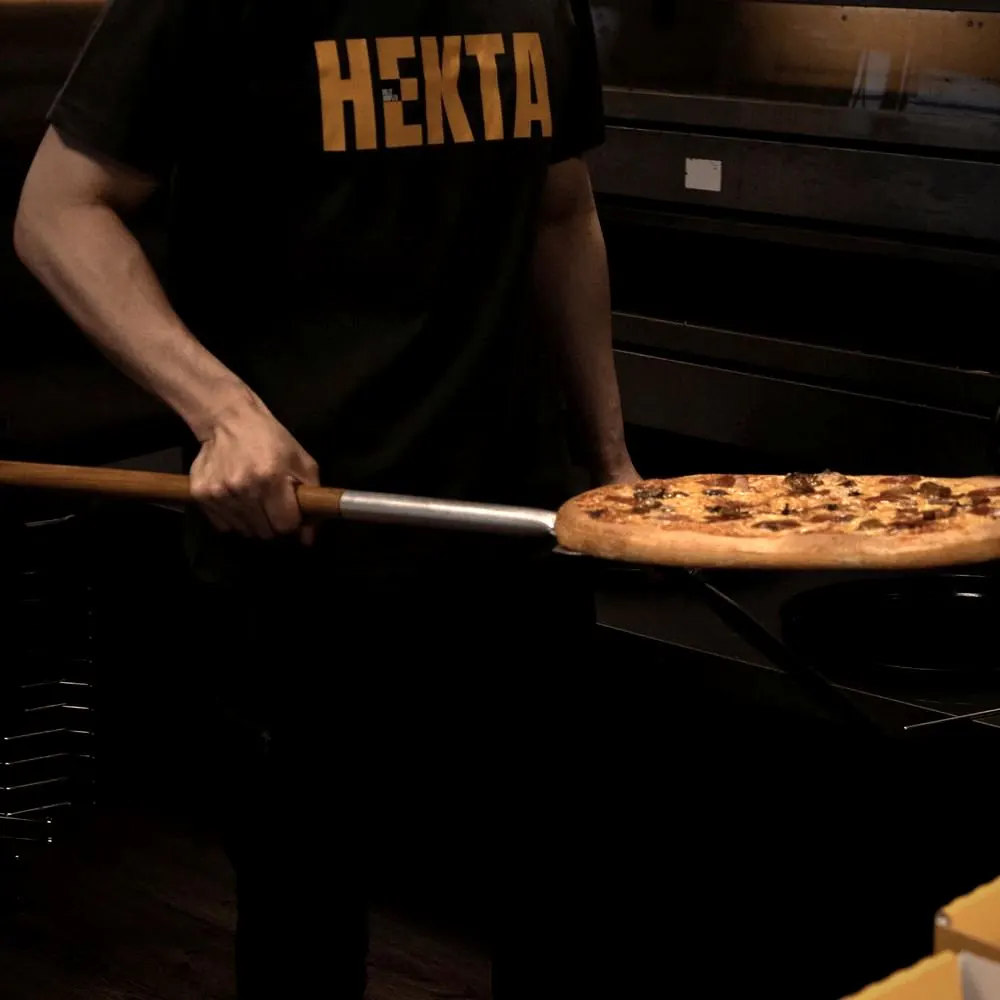 En pizzabaker i HEKTA-t-skjorte setter en pizza inn i ovnen