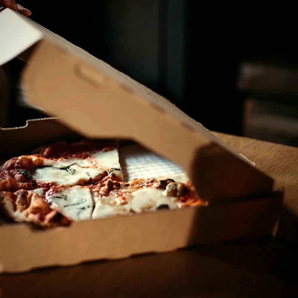 Hender åpner en pizzaeske med en pizza inni