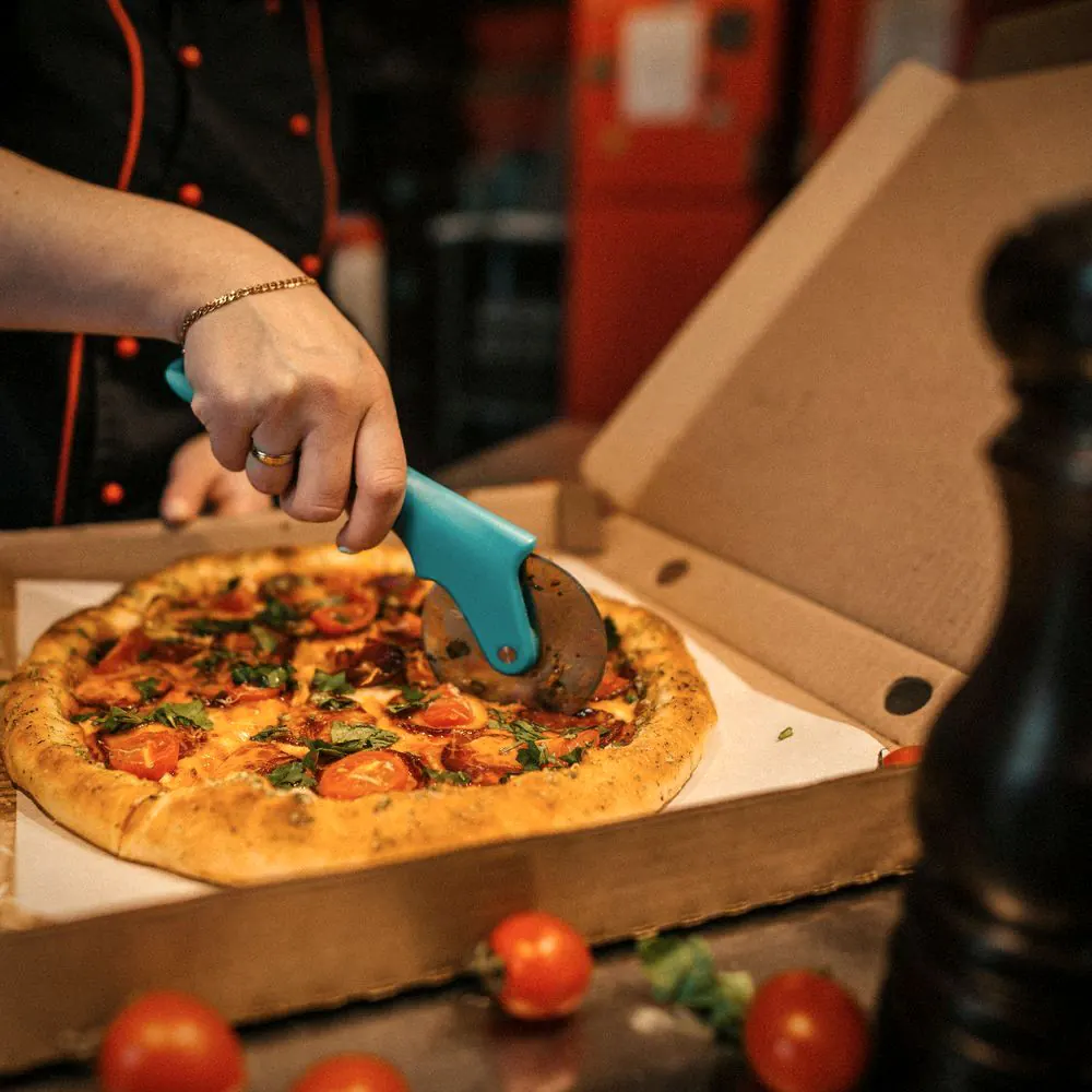 En pizza skjæres med pizzahjul i en åpen pizzaeske