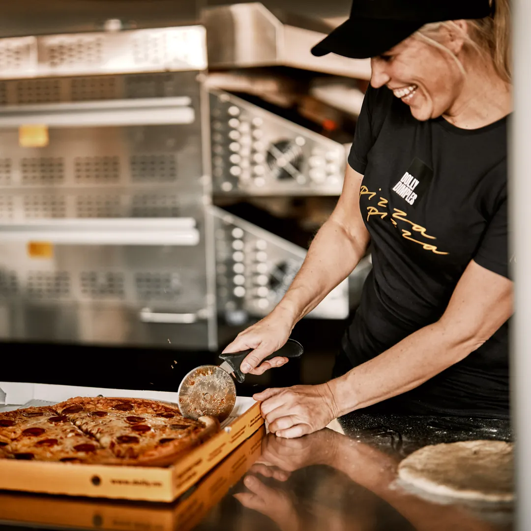 En smilende ansatt hos Dolly Dimples deler en pepperonipizza i en Dolly-eske