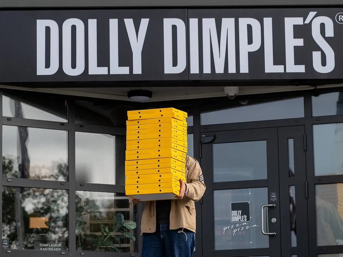 En person med en høy stabel gule Dolly-pizzaesker foran et Dolly Dimples-utsalg
