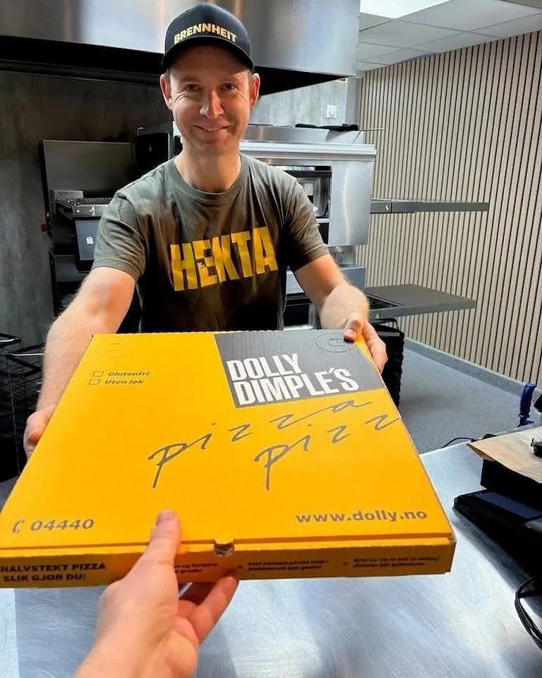 En ansatt hos Dolly Dimples rekker over en gul Dolly-pizzaeske