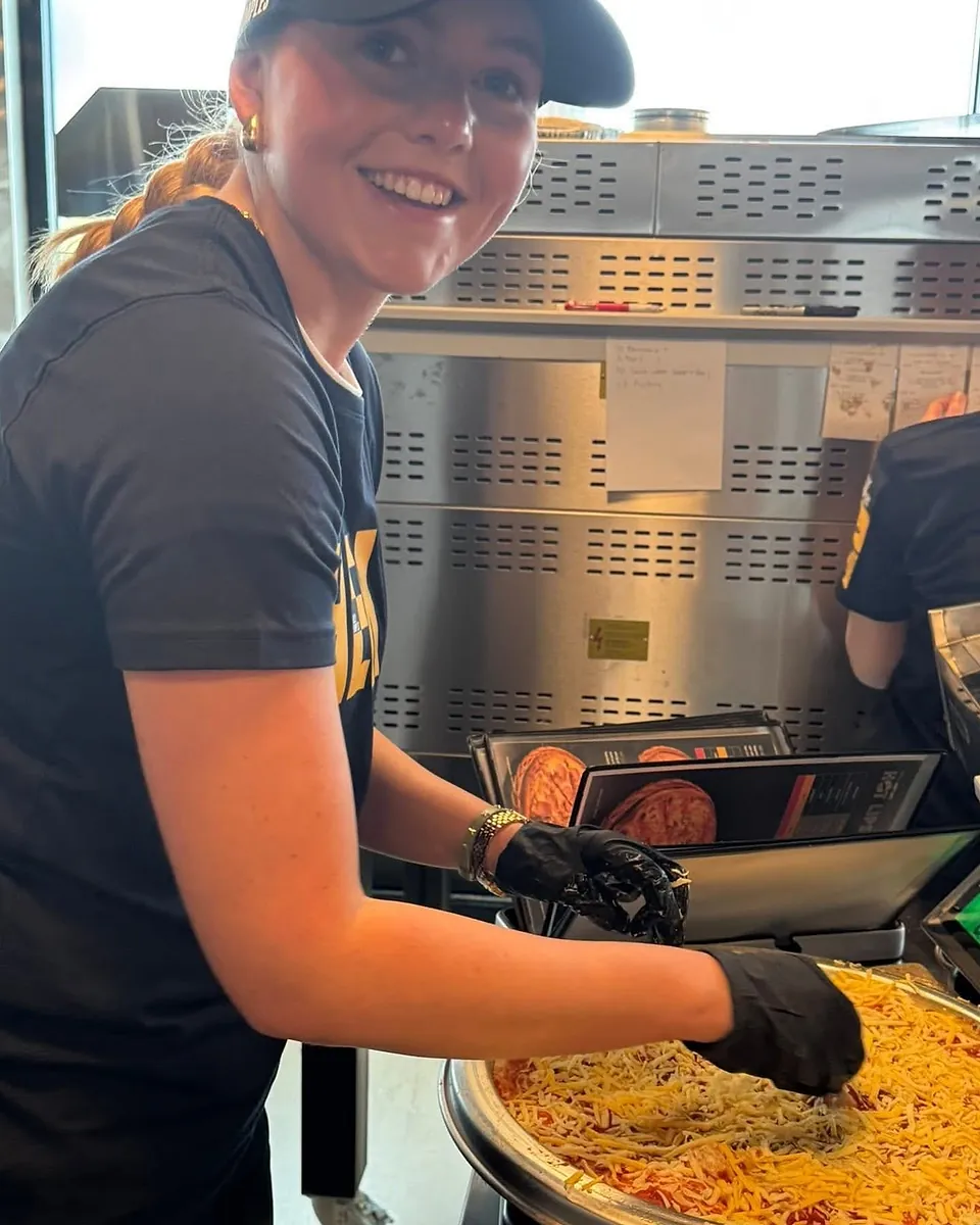 En smilende ansatt hos Dolly Dimples legger ost på en pizza