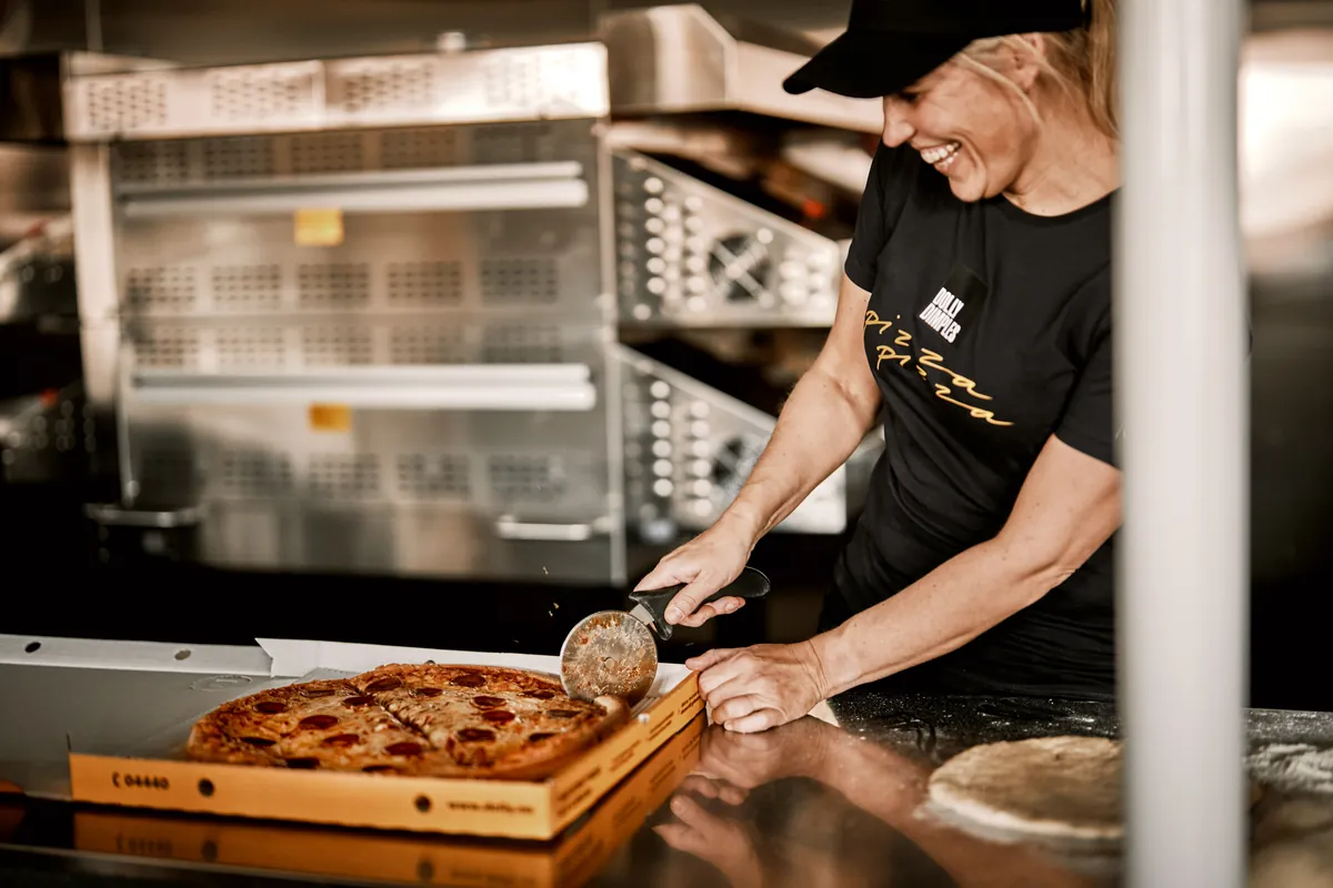En smilende ansatt hos Dolly Dimples deler en pepperonipizza i en Dolly-eske